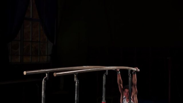 Male gymnast acrobat performs handstand on parallel bars in a dark room in slow motion