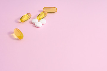 Yellow fish oil capsules and white pills with selective focus on pink background. Omega nutrition...