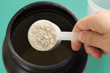 Whey Protein. Point of view of hand holding measuring scoop. Vanilla flavour. Color background:...