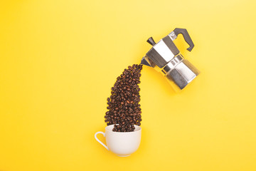 Coffee beans pouring from coffee maker into cup on yellow background. Love coffee concept....
