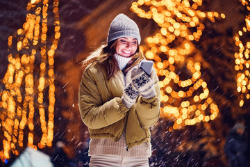A beautiful young woman or girl doing selfie or using phone emotionally outdoors in front of Christmas holidays decorations.