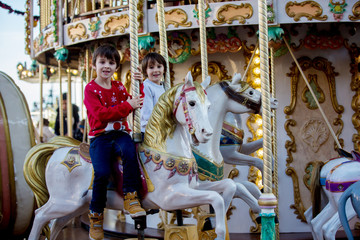 Sweet boys, brothers, riding in a Santa Claus sledge on a merry-go-round, carousel attraction in Europe, active children © Tomsickova