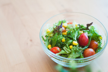A fresh and healthy salad made with fruits and vegetables in a bowl on a wooden background.