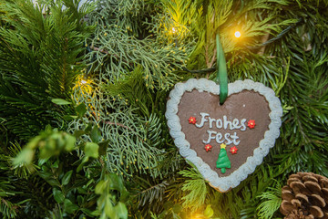 Lebkuchenherz mit der Aufschrift Frohes Fest und einem kleinen Weihnachtsbaum hängt an einem Weihnachtsstrauch.