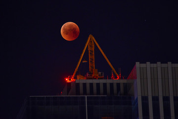 Construction crane on the background of a full red moon. Red moon, total lunar eclipse.