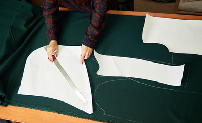 Close-up of female hands making chalk markings of paper patterns on green fabric copy space surface...