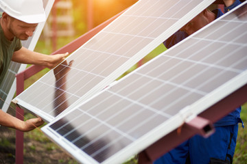 Team of technicians adjusting big shiny solar panel to metal platform on sunny summer warm day....
