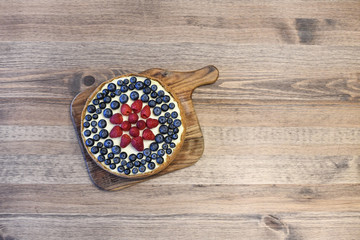 Fototapeta na wymiar Homemade cheesecake decorated with berries (blueberries and raspberries) on raw wood loft table