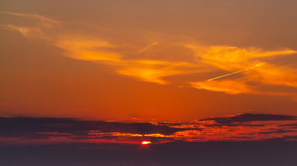 sky during a colorful, bright orange sunset, sun's rays make their way through the clouds