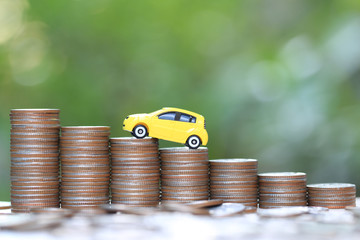 Miniature yellow car model on growing stack of coins money on nature green background, Saving money...