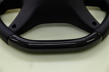 The disassembled from car steering part before installation of the equipment is a carbon black wheel with perforated genuine leather and tuning, stitched with a violet thread.