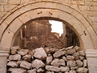 Pile of rocks blocking arched entrance with ruined building walls in the background, Qeparo, Albania