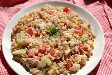 Cold salad with chicken, rice, various vegetables (tomato, pepper, cucumber, corn) and seasoning. Decorated with parsley leaves. Top view.
