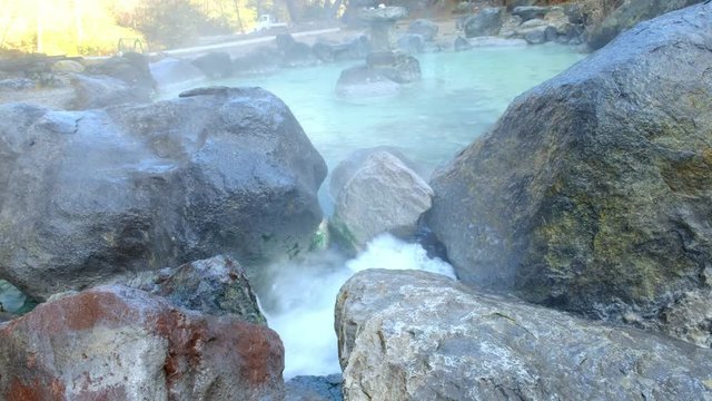 Waterfall from hot spring sources collected into a pool and hot water running down the valley in a warm stream in Kusatsu Onsen hot spring, Japan