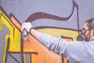 Street artist painting with a color spray can a graffiti on a wall outdoor - Urban man performing...