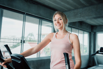 Woman workout elliptical trainer exercise in fitness gym., Portrait of pretty attractive caucasian woman doing elliptical trainer indoor gym., Beautiful girl in sportswear with smiling while workout. - obrazy, fototapety, plakaty