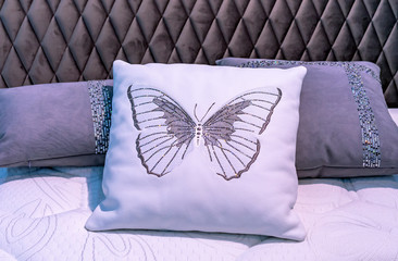 White leather pillow with embroidered butterfly in the bedroom interior.