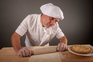 Mature chef rolling out pastry dough 