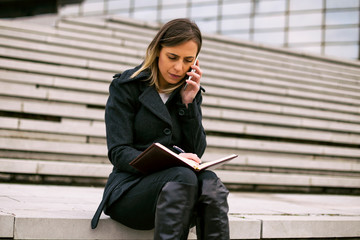 Businesswoman using phone and personal organizer while working outdoor.