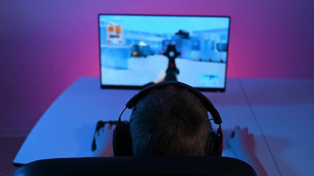 Rear view of boy sitting in front of pc playing FPS video game on computer