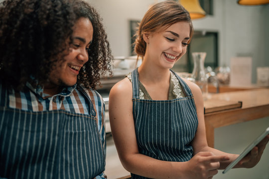 Two waiters smiling and laughing at something being pointed to on a digital tablet