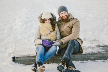 Fototapeta na wymiar Loving couple young people a man with a beard and a Caucasian woman are sitting on a wooden staircase in the winter on the snow St. Valentine's Day a date Christmas hugging and happy