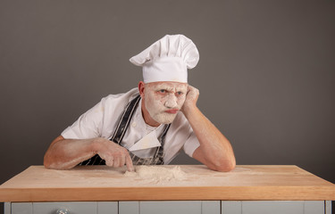 Mature chef covered in flour looking annoyed and fed up, resting on a table counter