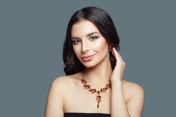 Jewelry model girl. Brunette woman with makeup, long hair and amber necklace and earrings on blue...