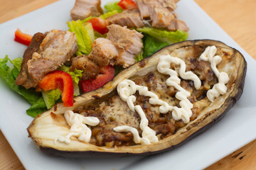 Cooked, baked eggplant stuffed with cheese, nuts, and yogurt dressing with fresh salad, in white plate. Healthy food.