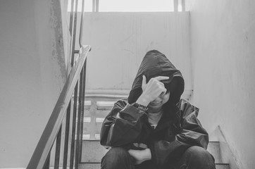 Portrait of sad young man covering his face with hands sitting on old stairs. Selective focus on hands. Sadness, despair, dark, concept