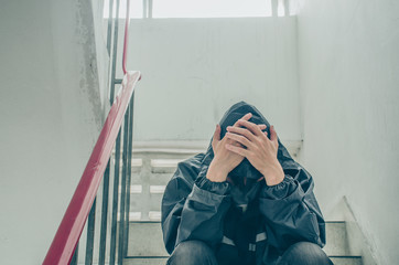 Portrait of sad young man covering his face with hands sitting on old stairs. Selective focus on hands. Sadness, despair, dark, concept