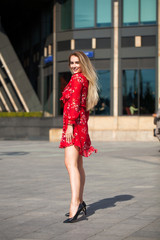 Sexy blonde model posing on th street in red summer dress