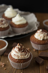 Chocolate cupcakes with whipped cream on rustic wooden table. Homemade dessert.