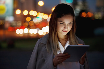 Beautiful woman with tablet outside in the night city