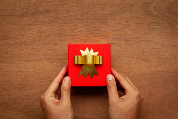 A man hands hold red gift box with golden ribbon on wooden table. Valentine day present background. Top view and copy space