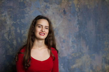 Fototapeta premium Smyling young girl in a red dress on a dark background