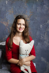 Naklejka premium Smyling young girl in a red dress holding lovely toy