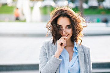 Closeup portrait of cute brunette girl with short hair walking in city.  She wears blue shirt, gray...