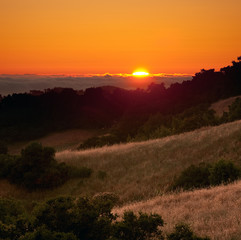 Sun setting behind fog over Pacific Ocean, from mountains of Coastal California