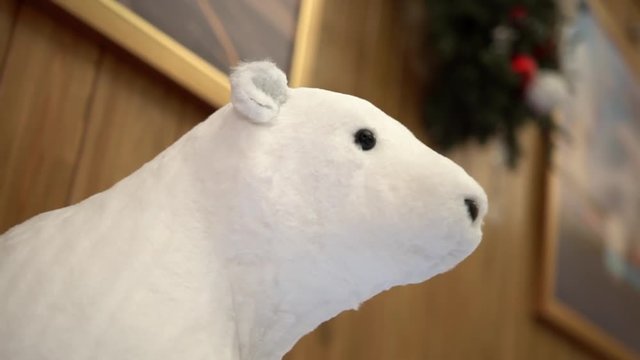 Fluffy white bear toy with black nose and eyes on wooden walls background in warm holiday atmosphere, close-up. Cute christmas decoration in cozy winter house.