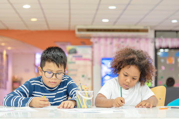 Little toddler girl and boy concentrate  drawing together.  Asian boy and Mix African girl learn and play together in the pre-school class. Children enjoy hand writing. Friendship in class.