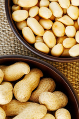 Peanuts in the shell and peeled close-up in cups. Roasted peanuts in their shells and peeled against a brown cloth.
