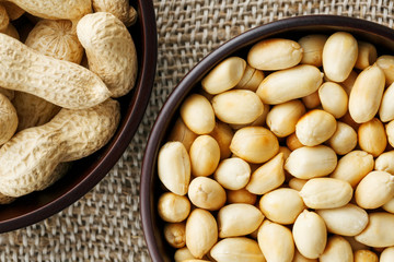Peanuts in the shell and peeled close-up in cups. Roasted peanuts in their shells and peeled against a brown cloth.