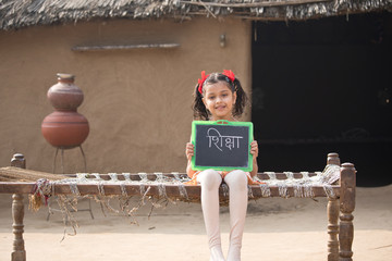 Rural Indian little girl holding slate at home
