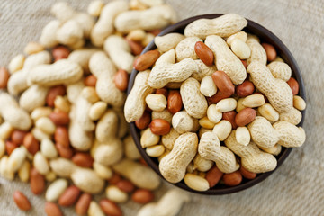 Peanuts in the shell and peeled close-up in cups. Roasted peanuts in their shells and peeled against a brown cloth.
