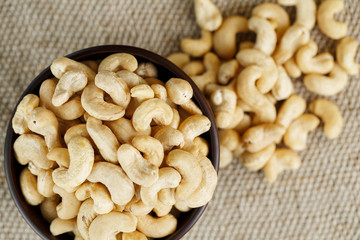 Cashew nuts in a wooden bowl on a burlap cloth background.