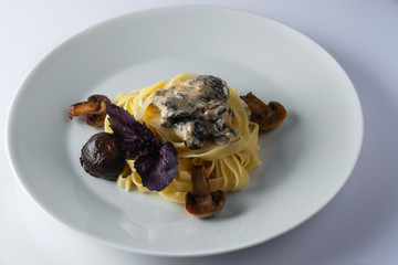 Pasta tagliatelle with creamy alfredo mushroom sauce on a white plate. Leaf of a basil. Close up. Selective focus.