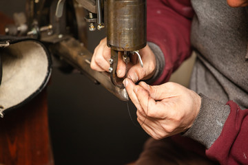 close-up of shoemaker's hands inserting thread into sewing machine