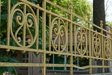 a fragment of an old yellow iron fence with a wrought pattern in the park