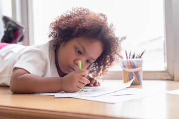 Little toddler girl laying down concentrate on drawing.  Mix African girl learn and play in the pre-school class. Children enjoy hand writing. 3 years girl enjoy playing at nursery.